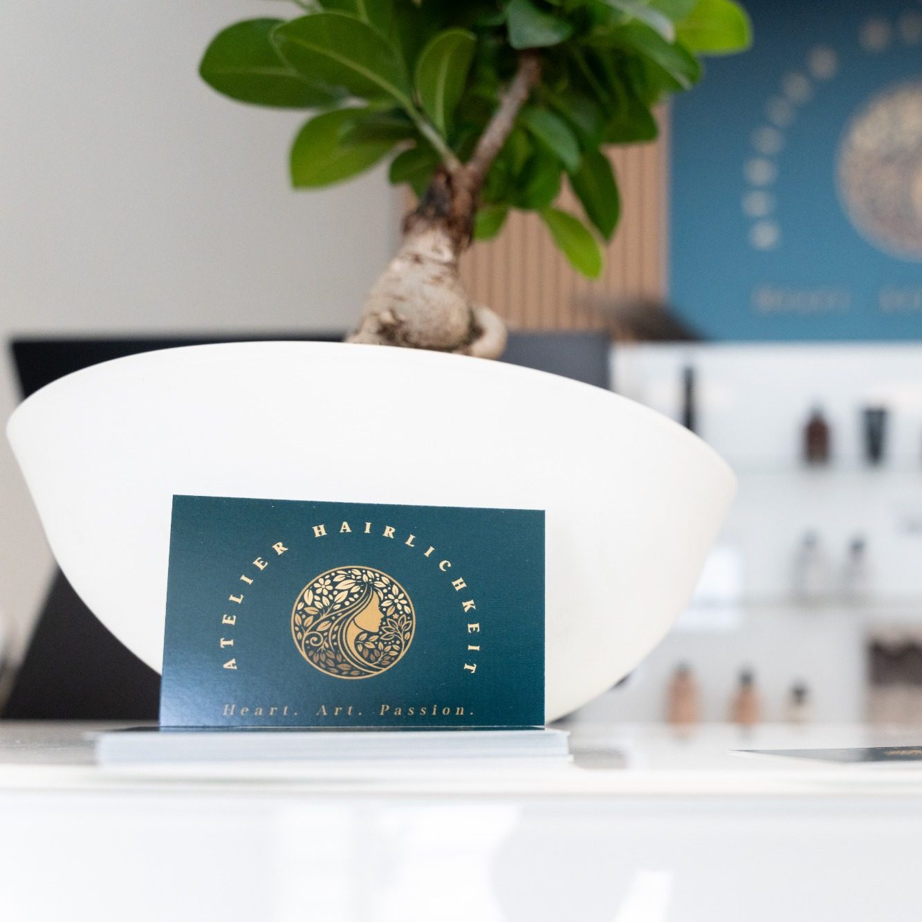Visitenkarte Firseur Atelier Hairlichkeit Bad Wörishofen Ein weißer Blumentopf mit einer Pflanze und einer dekorativen Visitenkarte im Hintergrund.
