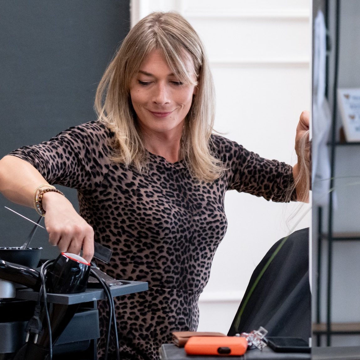 Friseur Bad Wörishofen Elly Frau mit blonden Haaren, die an einem Firseurtisch arbeitet, neben einer Pflanze.