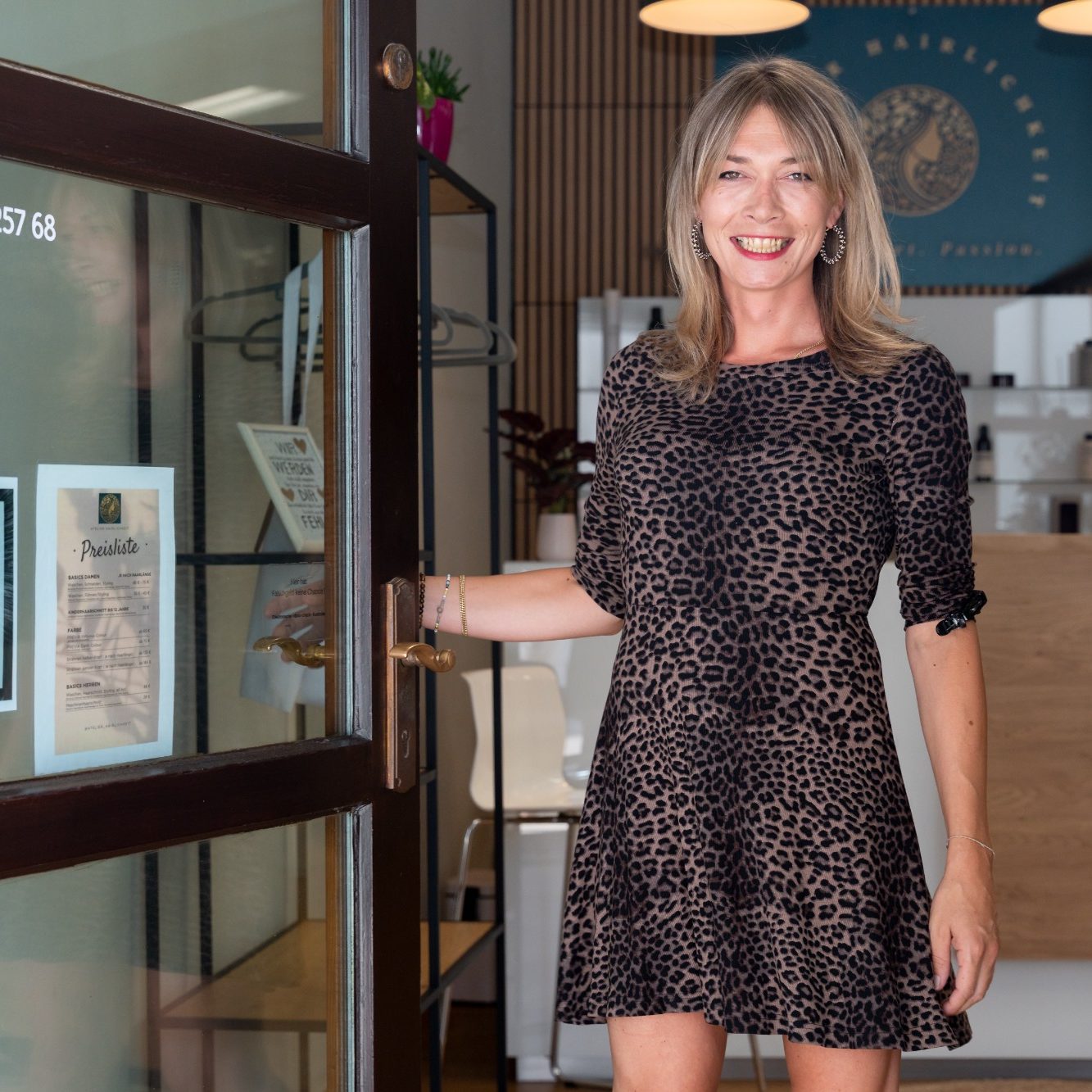 Friseurmeisertin Elly Frau in einem gepunkteten Kleid, die eine Glastür in einem modernen Friseur öffnet.
