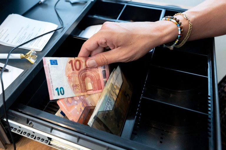 Faire Preise Eine Hand legt einen 10-Euro-Schein in eine Kassenschublade mit Geld.