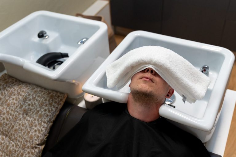 Wellness für den Mann Mann entspannt mit einem Handtuch über dem Gesicht in einem Friseursalon.